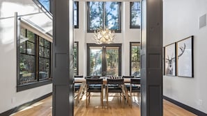 Een ruime kamer met een grote eettafel en stoelen, grote ramen en een kroonluchter.