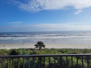 Ein Strand mit Wellen, blauem Himmel und etwas Grün im Vordergrund.