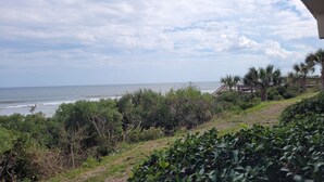 Paisagem costeira com vista para o mar, vegetação densa e uma estrutura de madeira com escadas descendo até a praia.