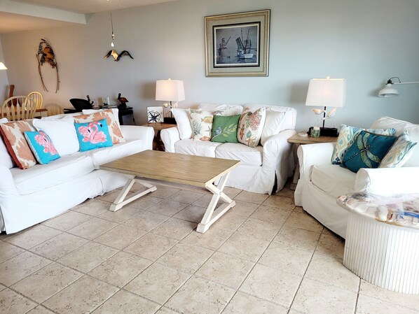 Una sala de estar con muebles blancos, una mesa de centro de madera y almohadones decorativos.
