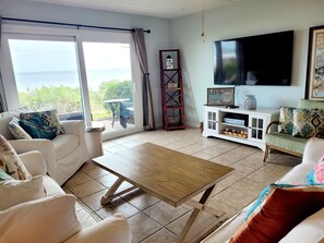 A living room with a large window, a flat-screen TV, and a wooden coffee table. - Directly facing the ocean, 2 Bedroom with Bunks for the kids! (ST. AUGUSTINE)