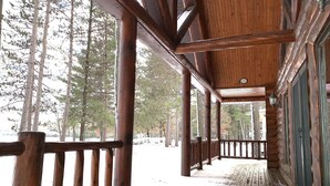 Una cabaña de madera con un porche cubierto y una terraza cubierta de nieve.