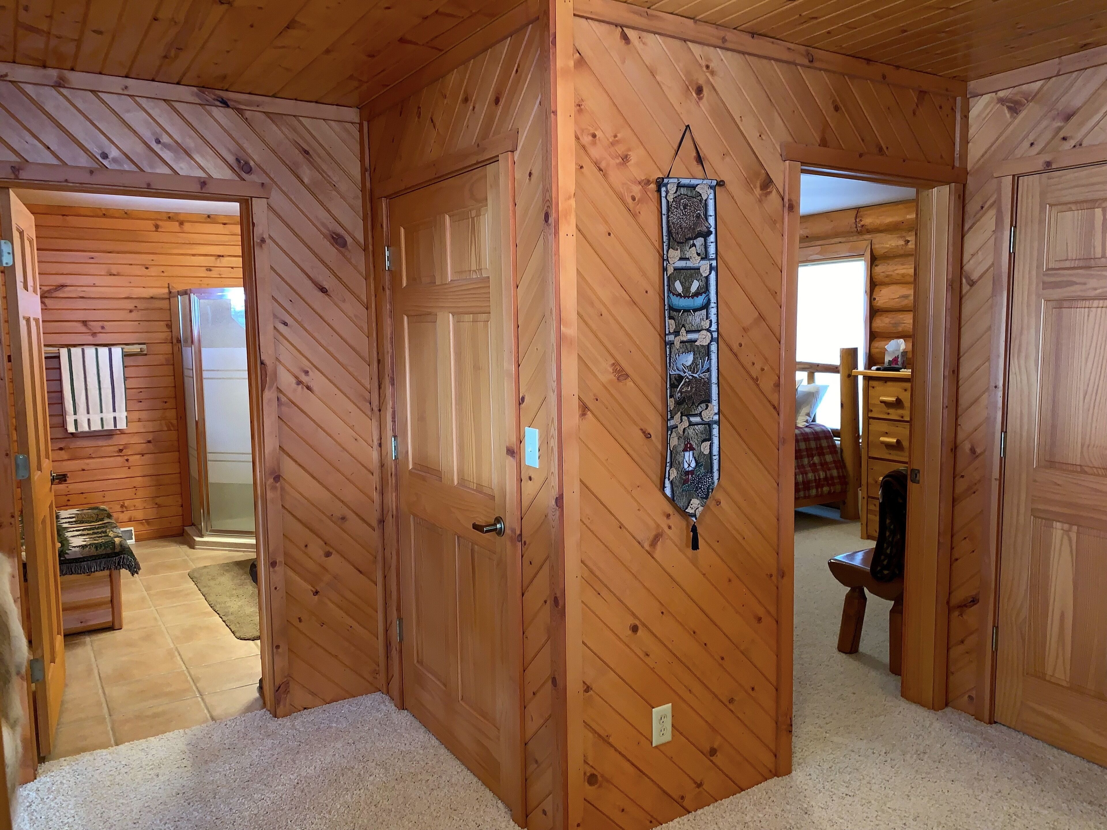 Interior de madera con una puerta que da al baño, un perchero y una pequeña mesa con una silla.