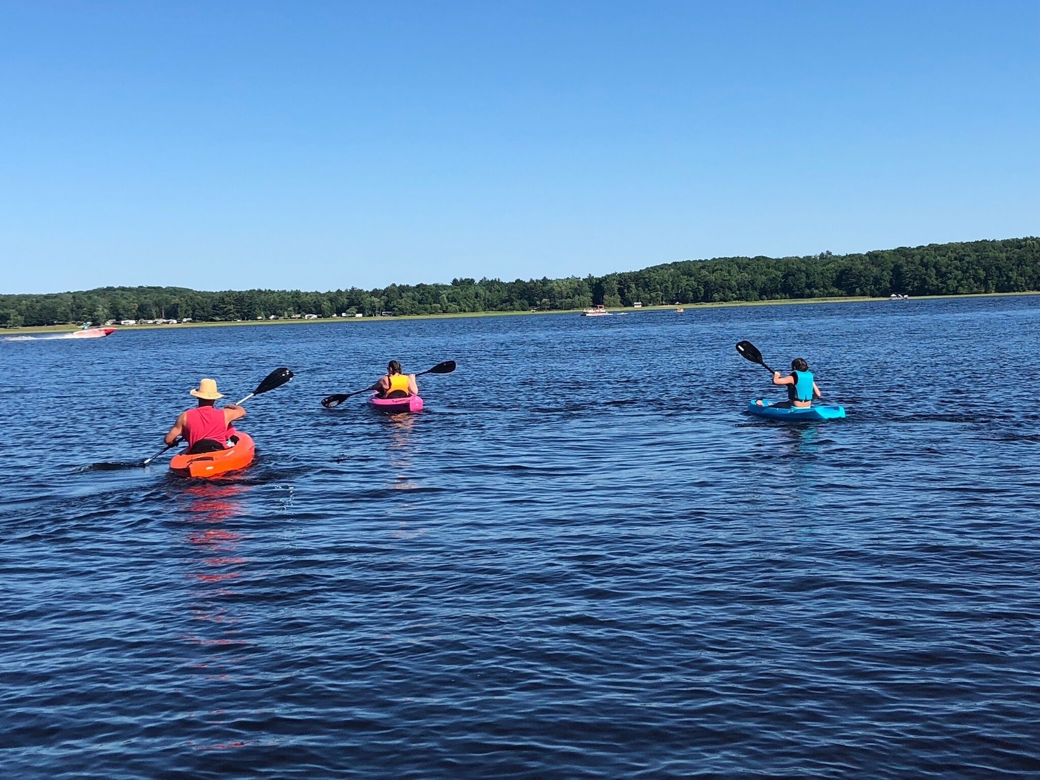 Three kayaks on a calm lake with a forested shoreline in the background.