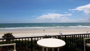 Une vue sur la plage depuis un balcon, avec une table et des chaises.