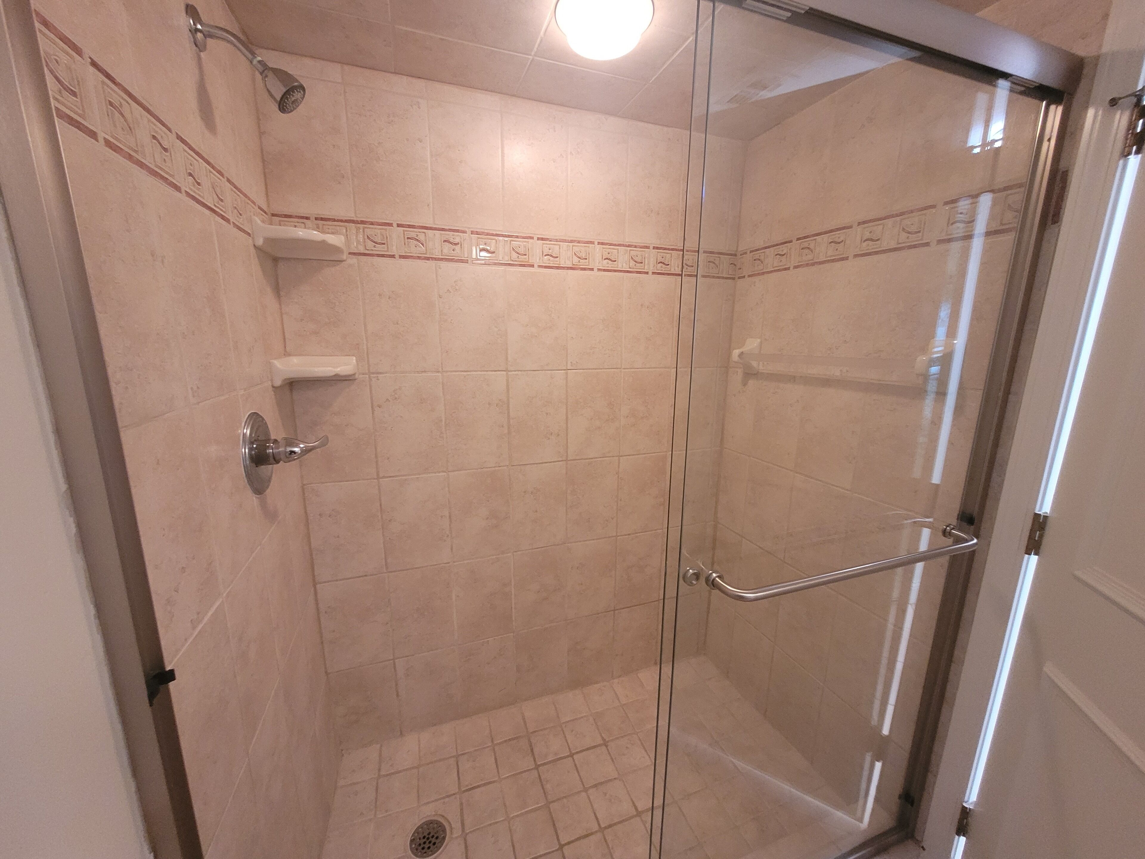 A glass-enclosed shower with a tiled floor and a showerhead.