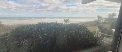 En utsikt från ett fönster med utsikt över en strand, en klar himmel, en sandstrand och lite vegetation.