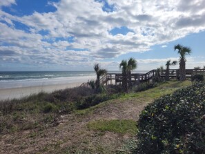 A beach with a wooden walkway leading to the ocean, surrounded by palm trees and vegetation.