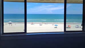 A beach view through a window with a view of the ocean and beachgoers. - Oceanfront 2 Bedroom Townhouse Summerhouse 209 (ST. AUGUSTINE)