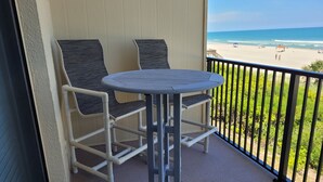 A balcony with a table and two chairs, overlooking a beach with umbrellas and people. - Oceanfront 2 Bedroom Townhouse Summerhouse 209 (ST. AUGUSTINE)