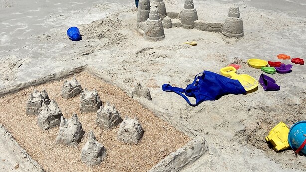 A sandy beach with a sandcastle and various beach toys.