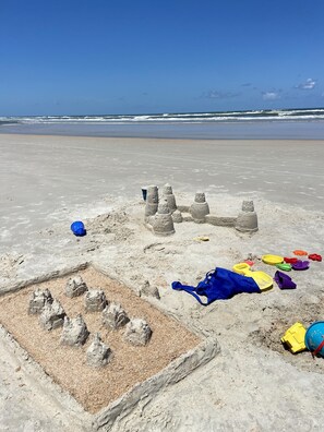 A sandy beach with a sandcastle and various beach toys.