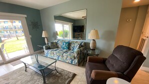Un salon comprenant un canapé, un fauteuil, une table basse en verre et une petite table d’appoint avec des lampes.