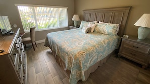 Une chambre à coucher avec un grand lit, deux tables de chevet avec des lampes, une commode et une fenêtre avec des stores.