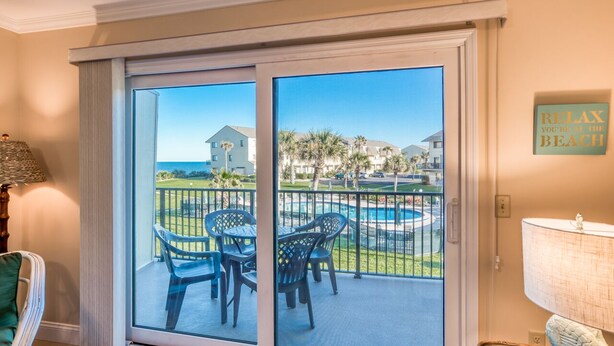 A balcony with a view of a pool and buildings, a chair, and a sign that reads "RELAX YOU'RE AT THE BEACH".