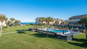 A pool area with a clear view of the ocean, surrounded by palm trees and modern buildings.