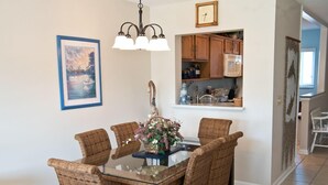 A dining area with a glass-top table surrounded by wicker chairs, a chandelier, and a clock on the wall.