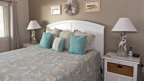 A bedroom with a bed, two nightstands, a lamp, a wall decoration, and a framed picture.