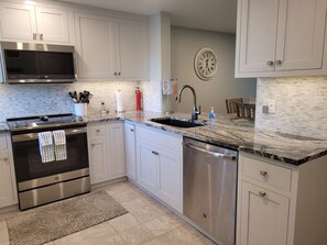 A modern kitchen with white cabinetry, a stainless steel range, a dishwasher, and a marble countertop.