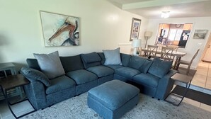Un salon avec un canapé d’angle, un pouf et un tapis.