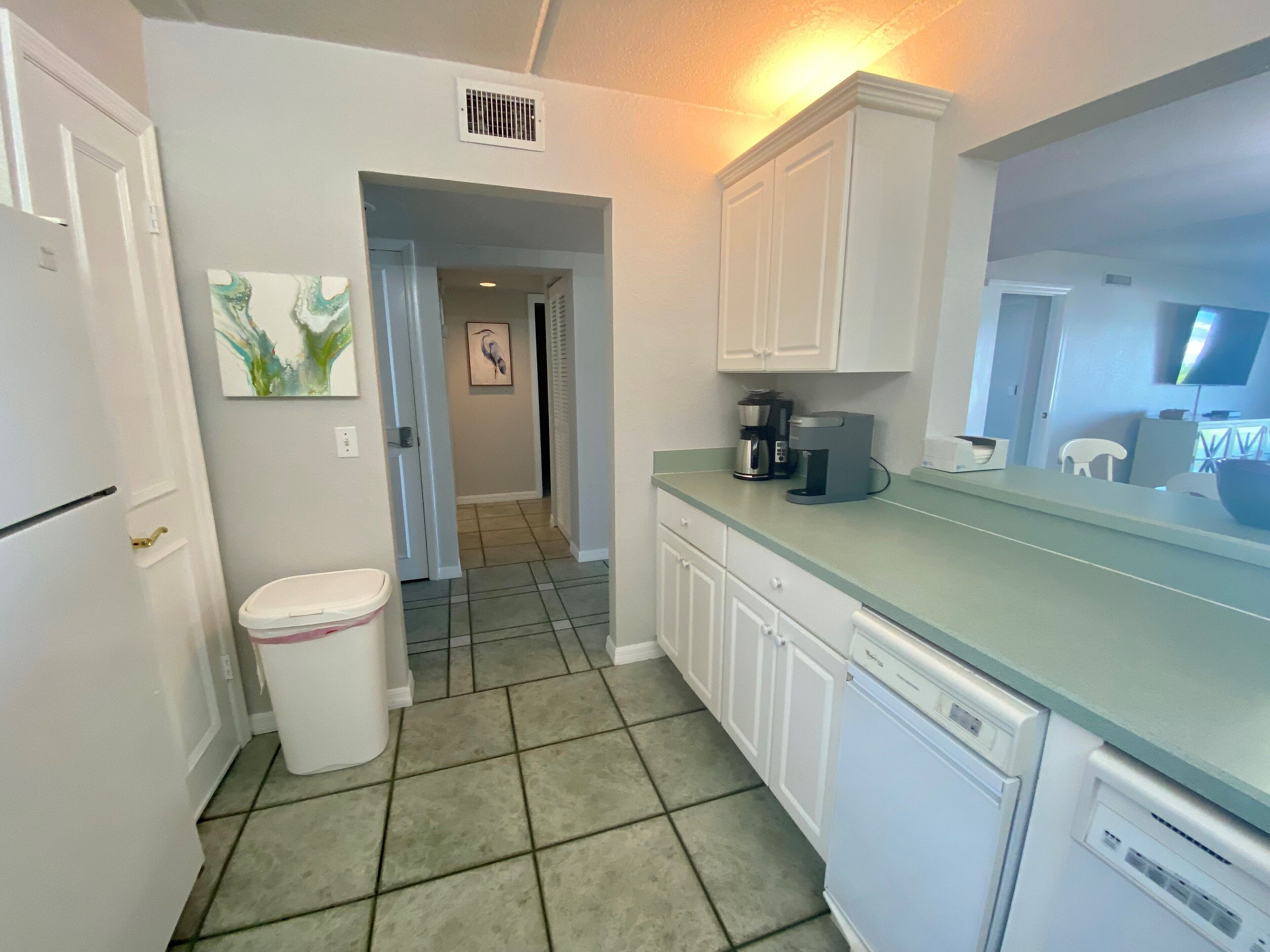 A kitchen with white cabinets, a coffee maker, and a trash can.