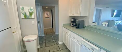 A kitchen with white cabinets, a coffee maker, and a trash can.