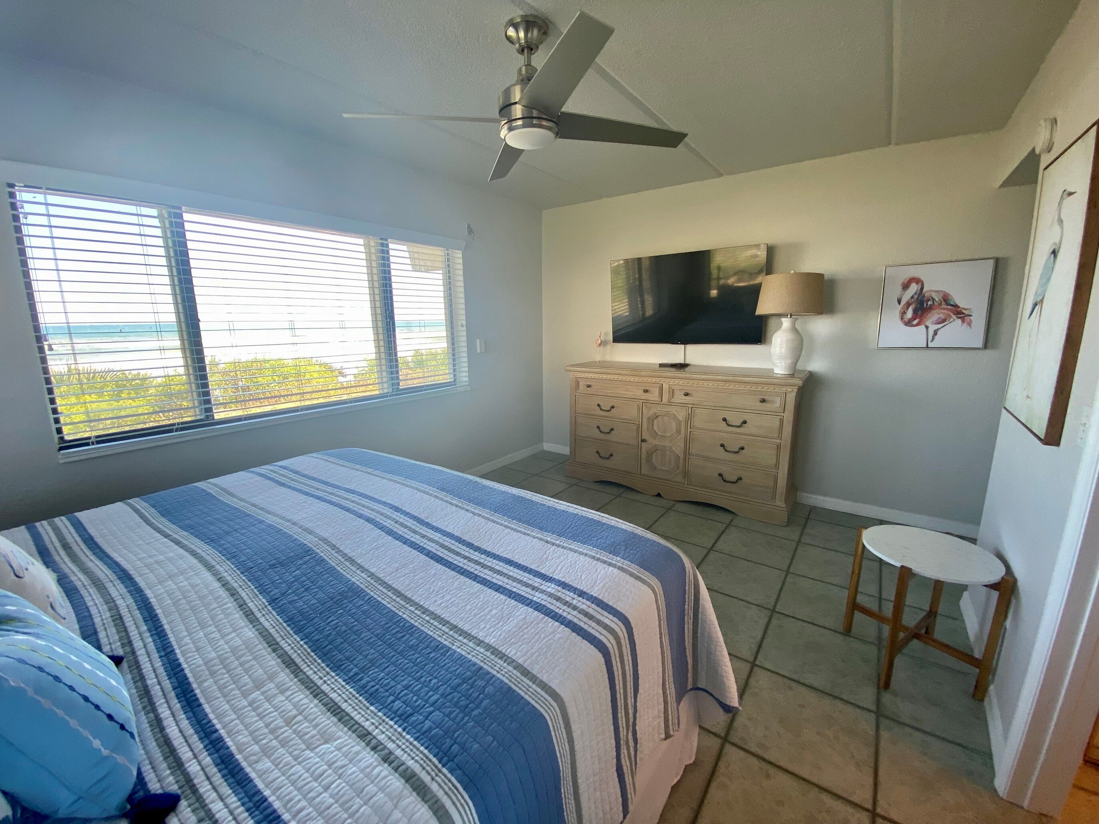 Une chambre à coucher avec un lit, une commode, un téléviseur et un ventilateur de plafond.