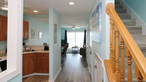Un couloir mène à une salle à manger équipée de meubles de rangement en bois et d’un escalier avec des rampes en bois.