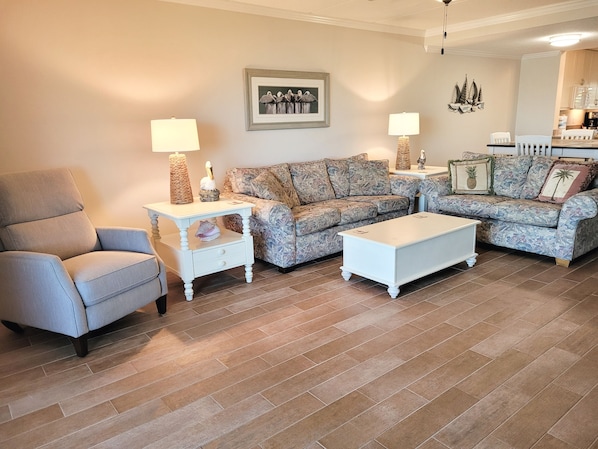 Relax in this stylish living room with a comfortable armchair, sofa, and coffee table, surrounded by artwork and decorative accents.