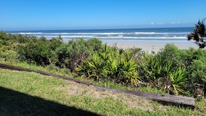 Una playa con olas del océano, vegetación verde y un cielo despejado.
