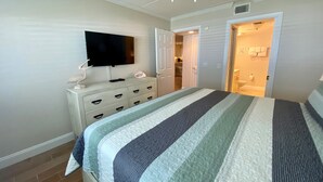 Un dormitorio con cama, cómoda, televisor y puerta abierta que da al baño.