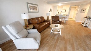Una sala de estar con un sofá de cuero marrón, un sillón blanco, una mesita redonda y una lámpara sobre una mesita auxiliar.