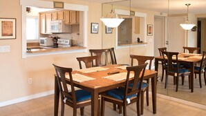 A dining area with a wooden table and chairs, a kitchen in the background, and a large mirror reflecting the room. - Oceanfront 2 Bedroom Flat Summerhouse 301 (ST. AUGUSTINE)
