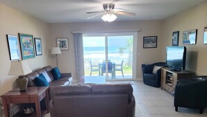 A living room with a sofa, a TV, and a view of the ocean through the sliding glass door. - Oceanfront 2 Bedroom Flat Summerhouse 301 (ST. AUGUSTINE)