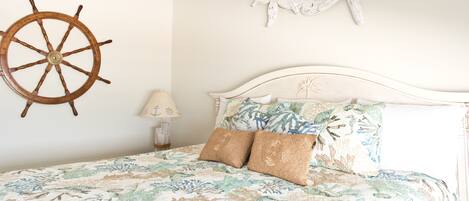 A bed with a floral bedspread, two pillows, a wooden ship wheel, a starfish decoration, and a lamp on a nightstand.