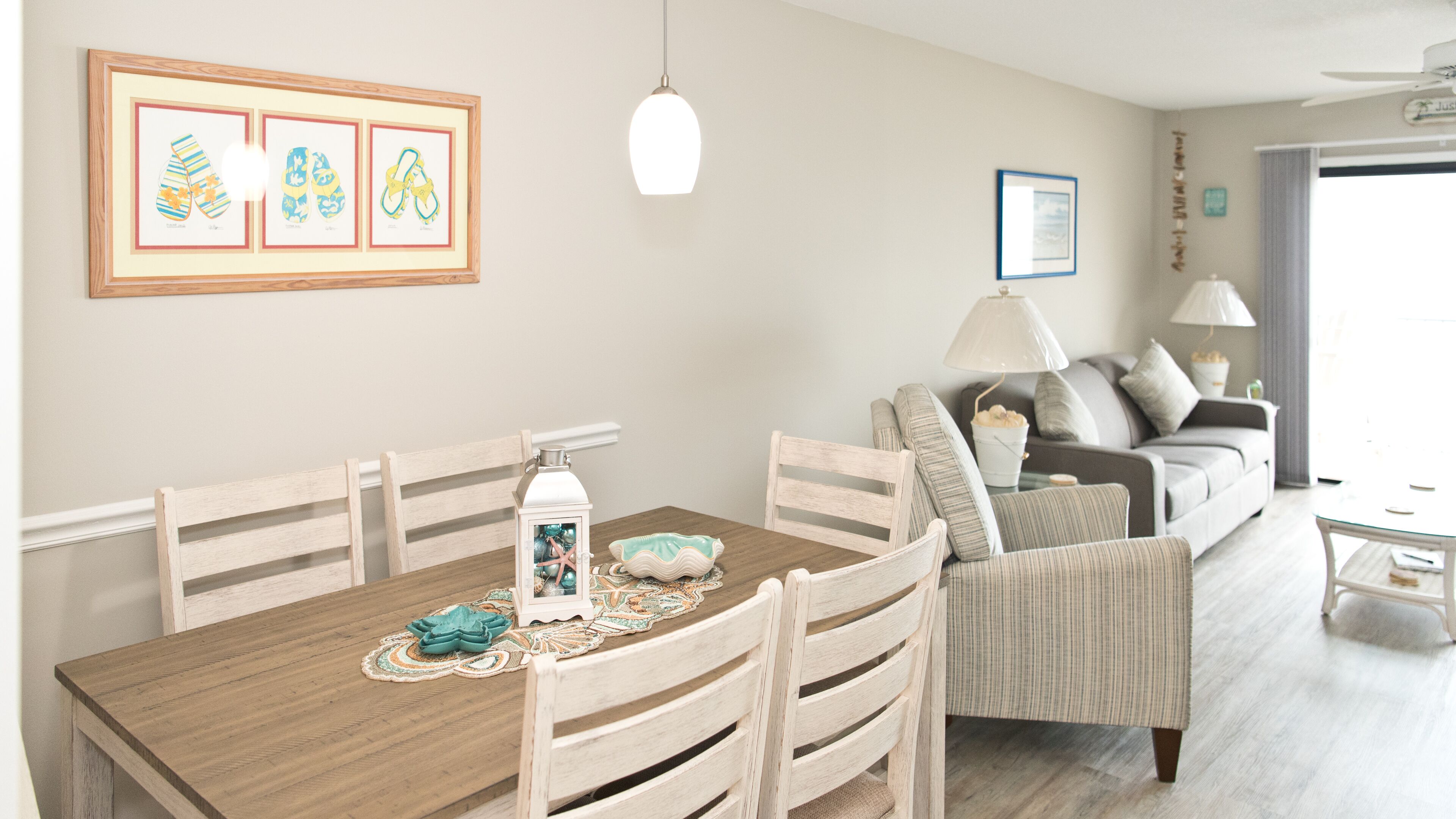 A dining area with a wooden table, chairs, and a decorative lantern. There is a sofa and a lamp in the background.