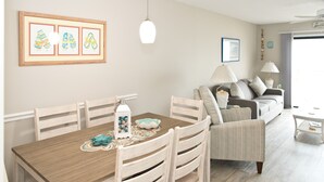 Un comedor con una mesa de madera, sillas y un farol decorativo. Se observa un sofá y una lámpara al fondo.