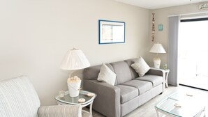 Una sala de estar moderna con un sofá gris, dos mesas auxiliares, una mesa de centro de vidrio y una lámpara.