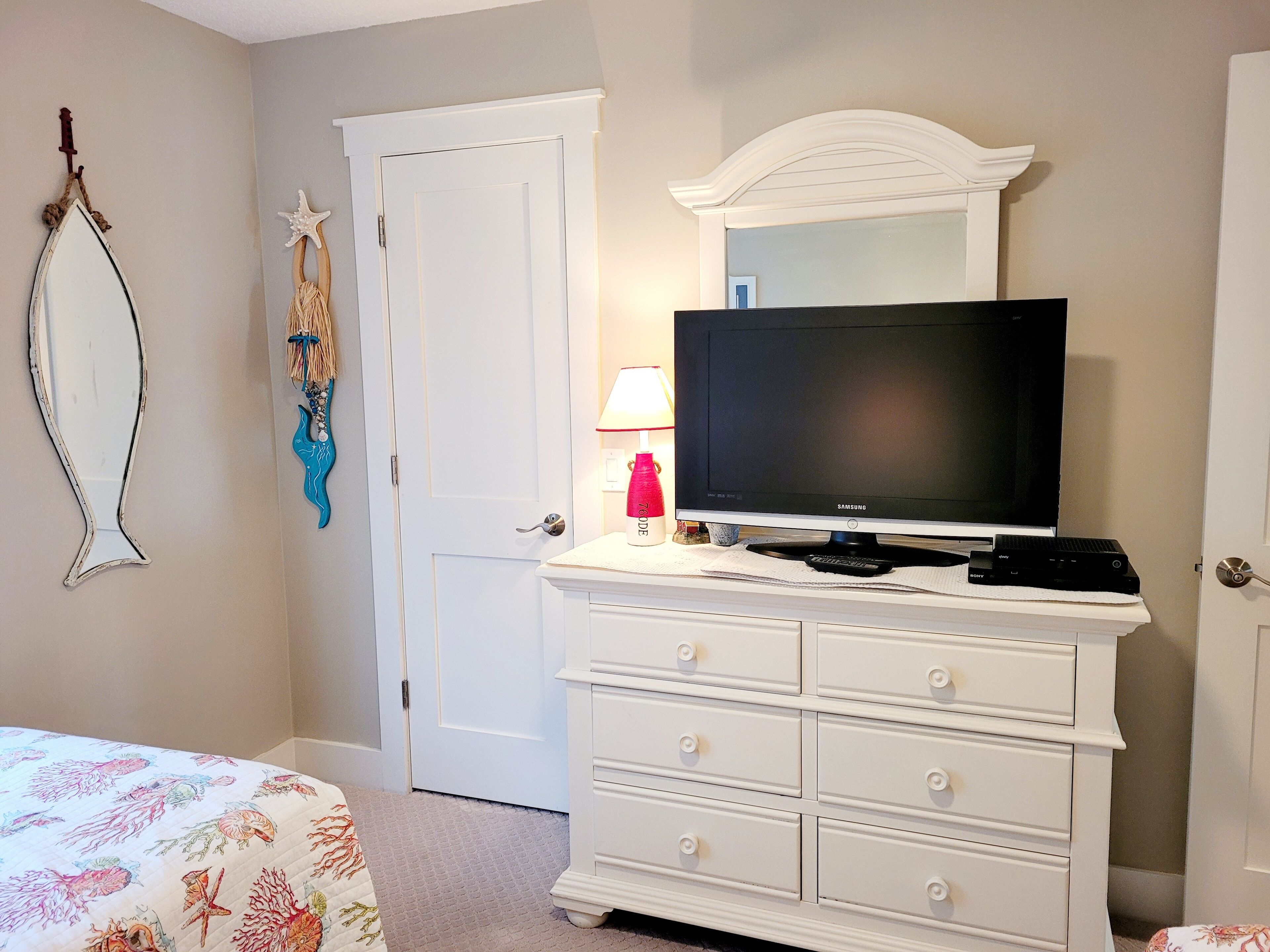 Un dormitorio con cama, cómoda, televisor y puerta.