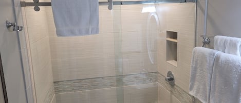 En moderne bruseniche med glasdør, et håndklædetørrestativ og en lille hylde.