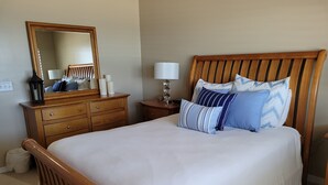 A neatly made bed with a wooden headboard, a dresser with drawers, a mirror, and a bedside lamp. - Oceanfront 2 Bedroom Townhouse Summerhouse 305 (ST. AUGUSTINE)