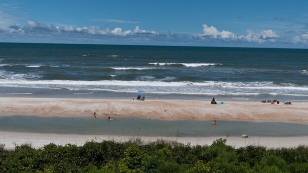 A beach with people sunbathing and swimming, a clear sky, and waves crashing onto the shore. - Oceanfront 2 Bedroom Townhouse Summerhouse 305 (ST. AUGUSTINE)