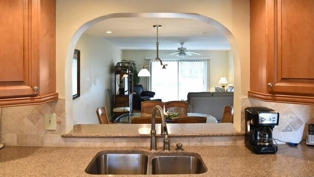 A kitchen with granite countertops, stainless steel sink, wooden cabinets, and a ceiling fan. - Oceanview 2 Bedroom Flat Summerhouse 319 (ST. AUGUSTINE)