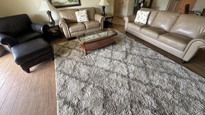 A living room with a black leather sofa, a beige leather sofa, and a beige armchair. There is a glass coffee table in the center. - Oceanview 2 Bedroom Flat Summerhouse 319 (ST. AUGUSTINE)