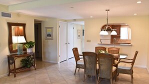 A dining area with a round table and six wicker chairs, a wooden console table with a lamp and plants, and a kitchen area with a large mirror and pendant lights. - Oceanview 2 Bedroom Flat Summerhouse 319 (ST. AUGUSTINE)