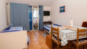 A small, compact room with two beds, a dining table, a TV, and a window with curtains. - Studios Nina (Split)