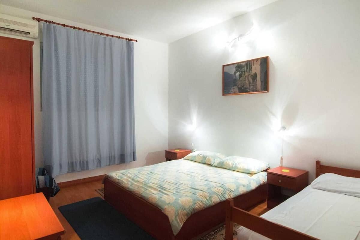 A bedroom with a bed, bedside tables, a nightstand, a window with curtains, and a wall-mounted picture.