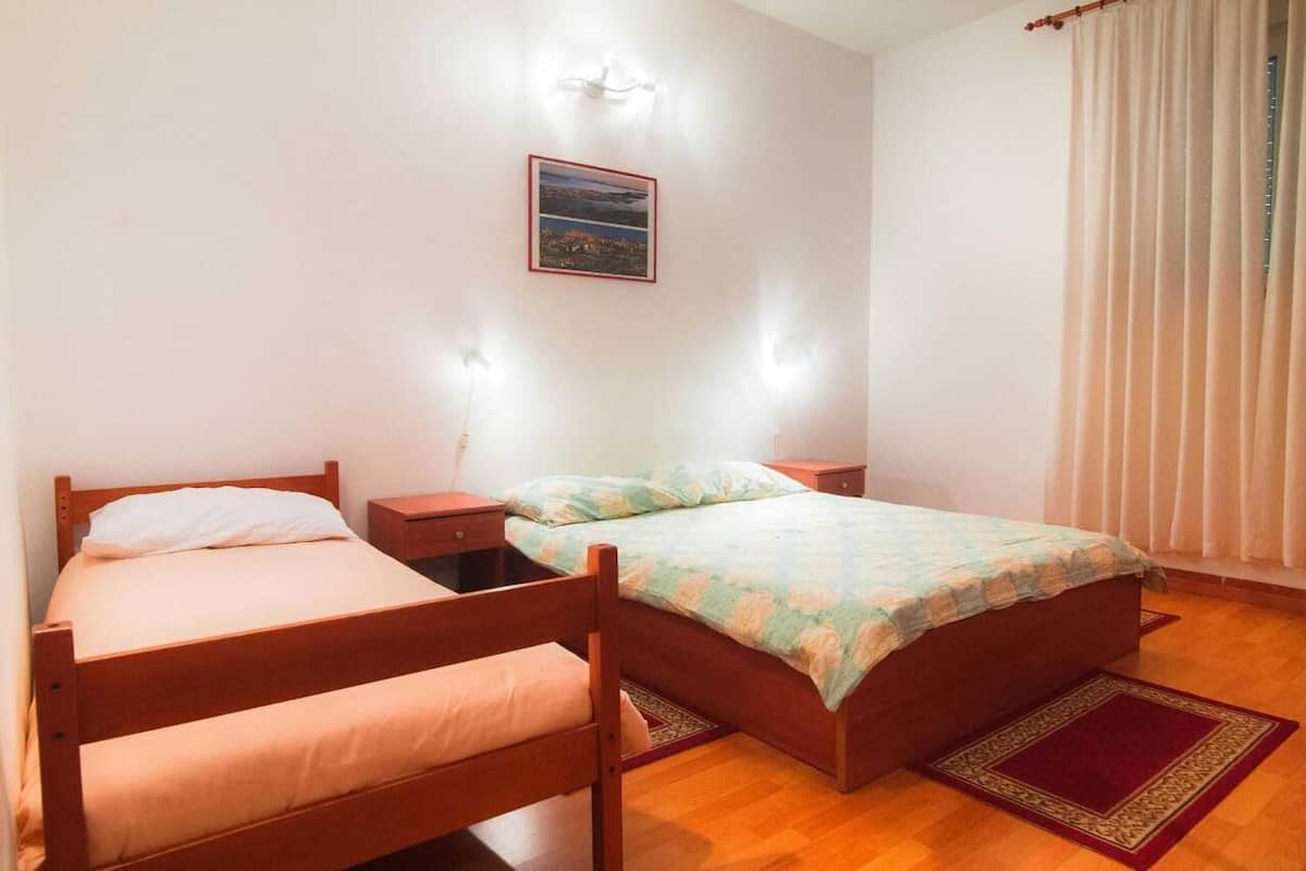 A room with two wooden beds, a nightstand, a wall-mounted light, and a window with curtains.