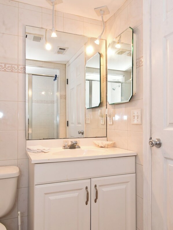 Une salle de bain avec un meuble-lavabo blanc, un grand miroir et une douche visible au fond.