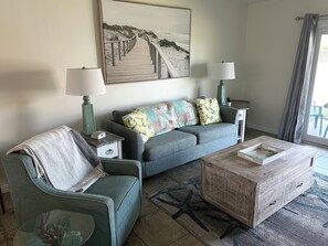 A living room with a sofa, armchair, coffee table, and a painting of a beach. - Tier 3. Oceanview 2 Bedroom Flat Summerhouse 340 (ST. AUGUSTINE)